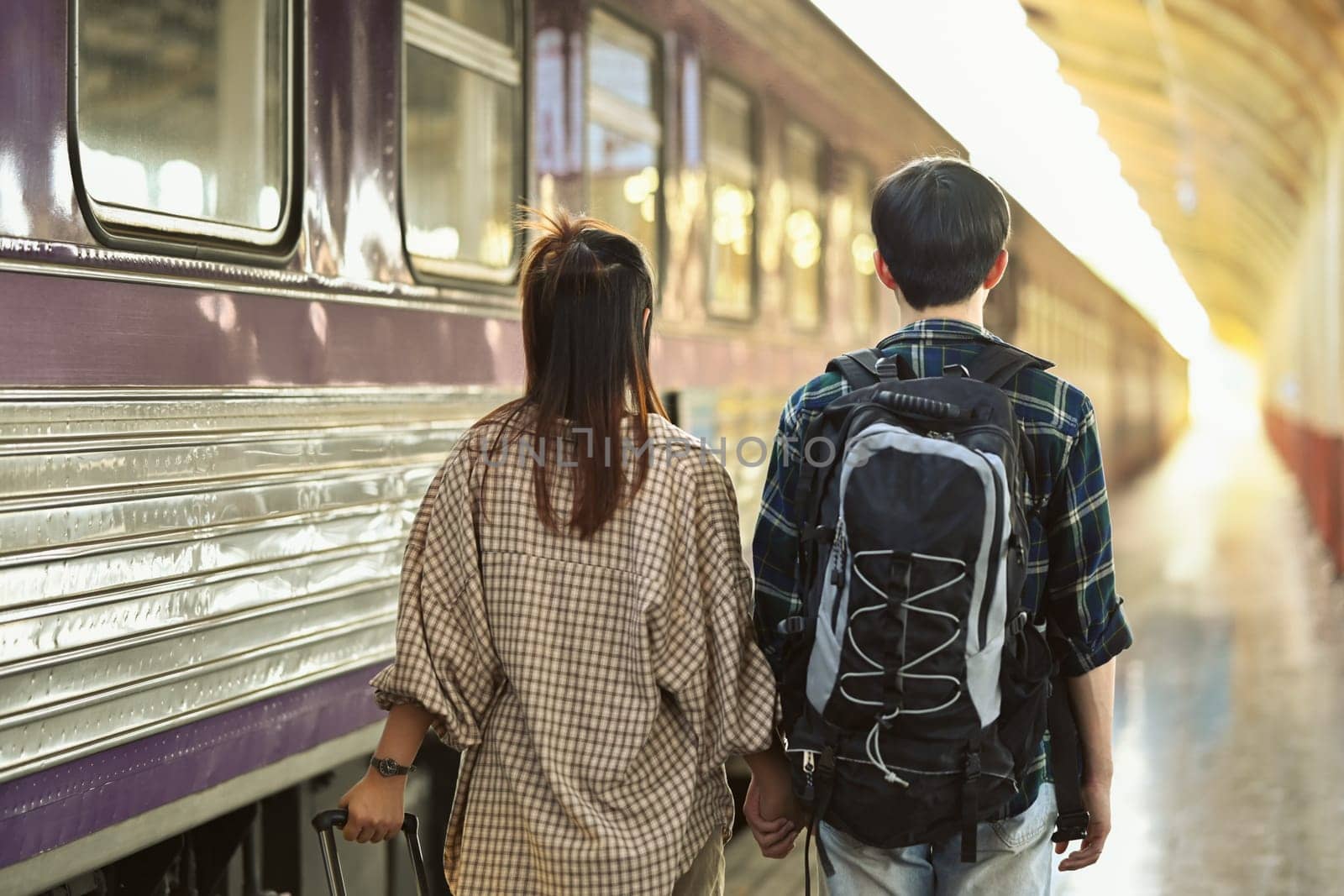 Rearview of young couple walking at the train station platform. Travel and vacations concept by prathanchorruangsak