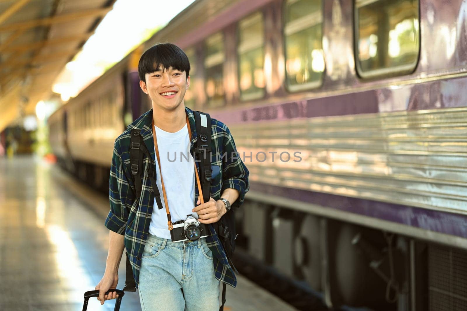 Portrait of happy young man walking in a train station with with suitcase. Traveling and vacations concept.