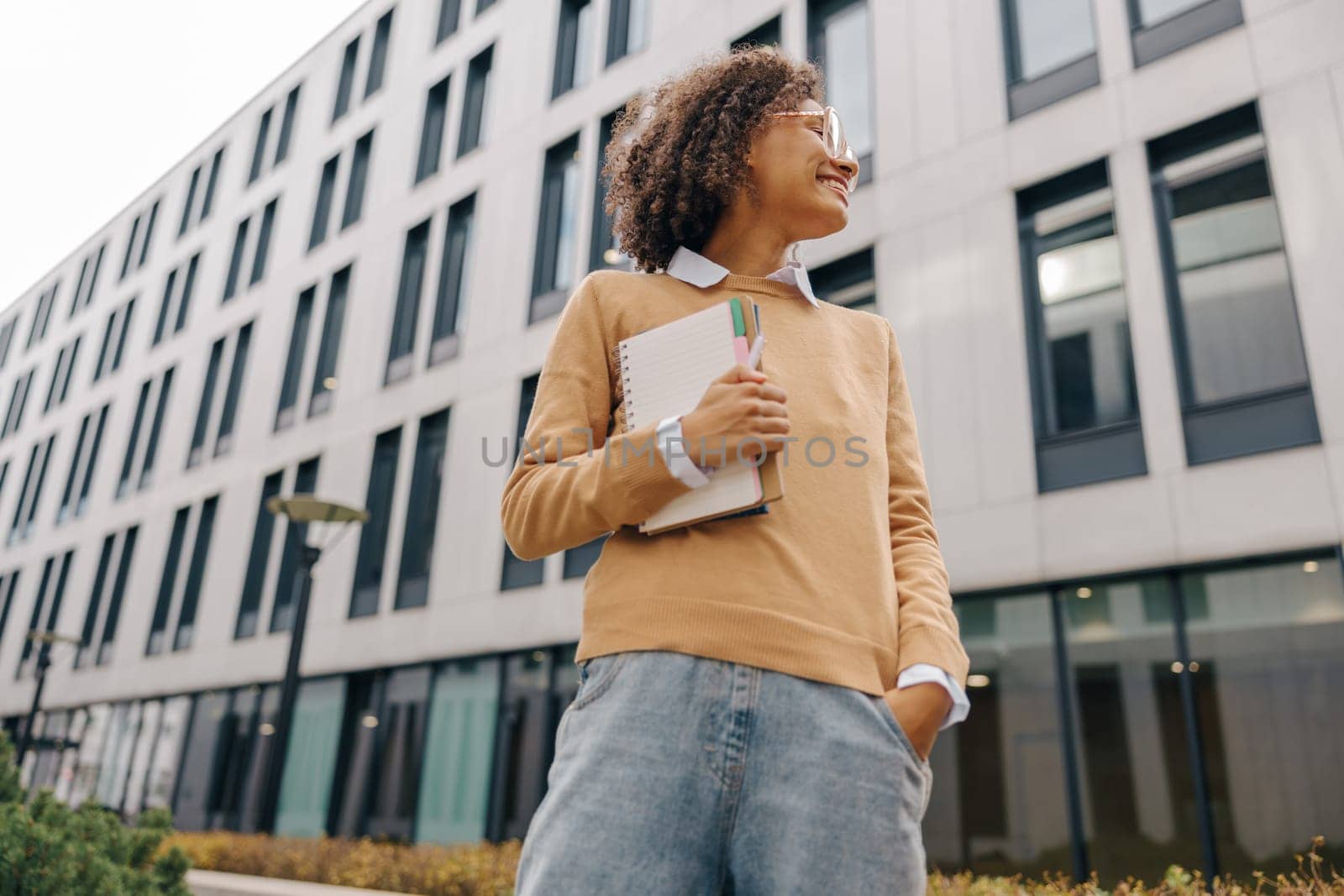 Young female student standing with note pads on modern building backgrounds