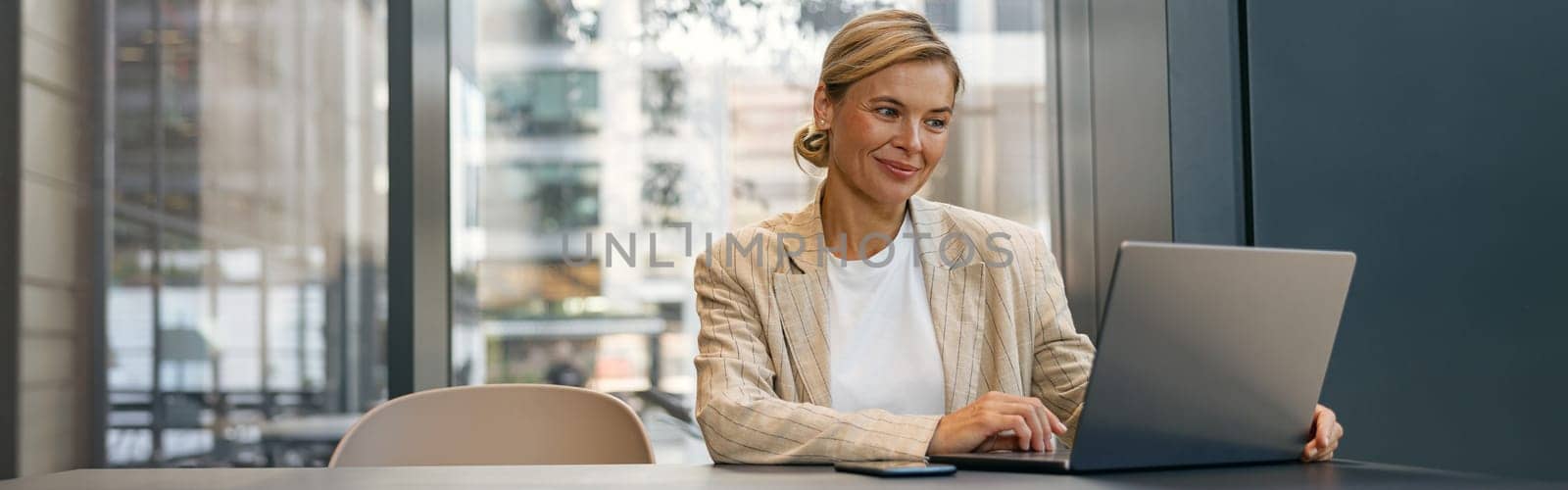 Stylish business woman working on laptop sitting the desk on office background