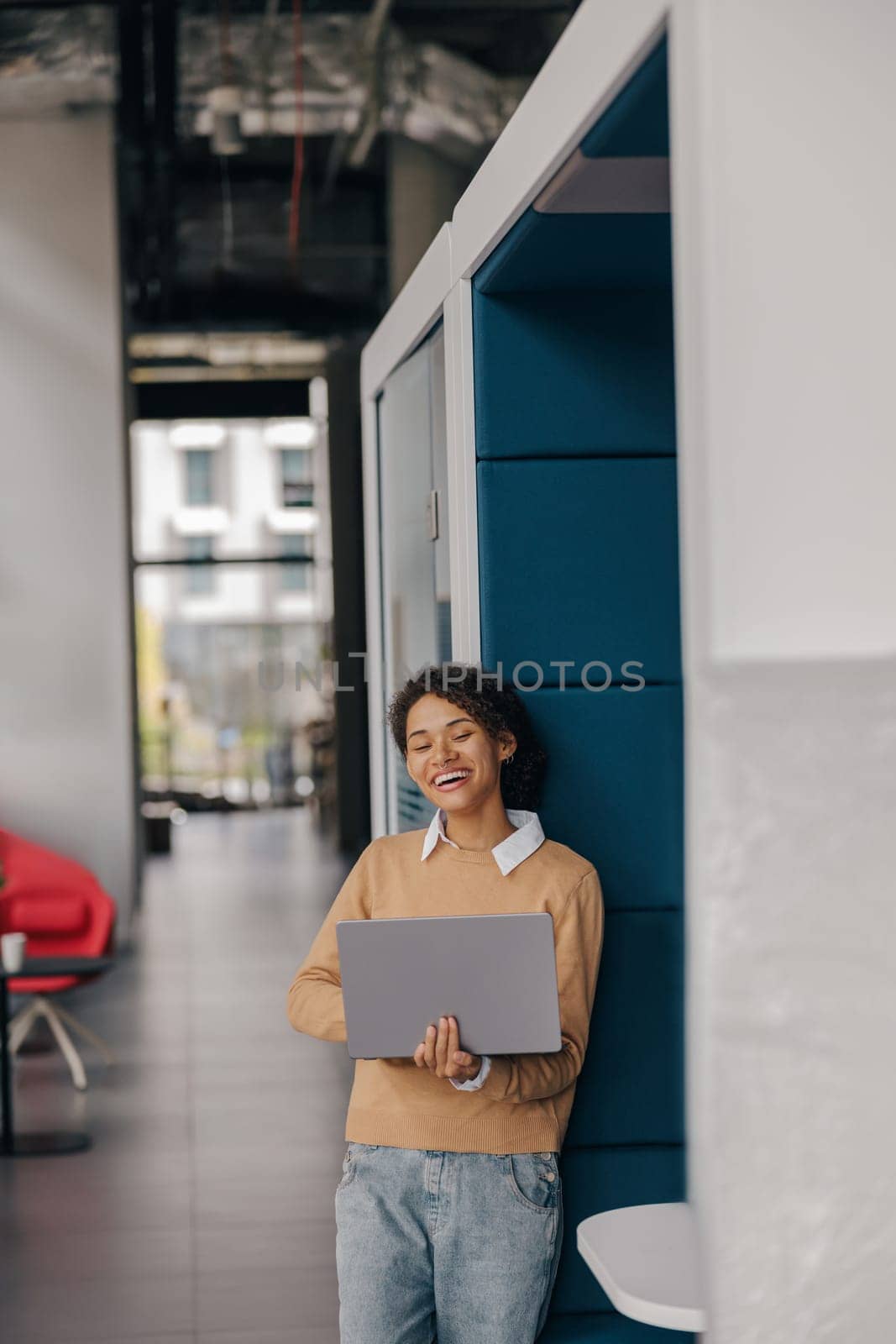 Smiling female entrepreneur using laptop while standing on office background and looks camera by Yaroslav_astakhov