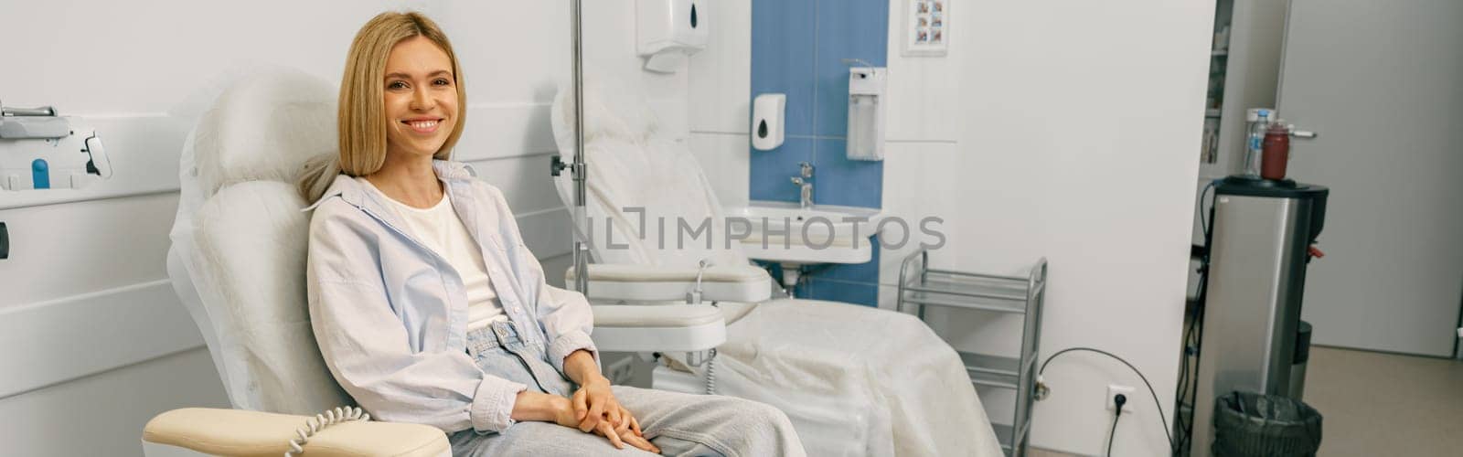Smiling woman sitting in armchair while waiting for IV infusion during treatment in hospital by Yaroslav_astakhov