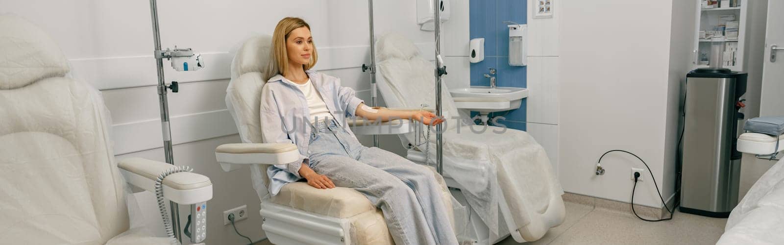 Pretty woman patient sitting in armchair while receiving IV infusion during treatment in hospital by Yaroslav_astakhov