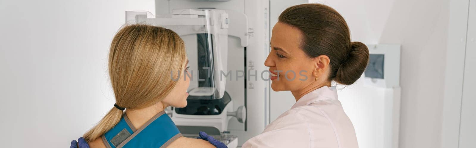 Smiling doctor prepairing woman before doing mammogram x-ray to check for breast cancer at hospital by Yaroslav_astakhov