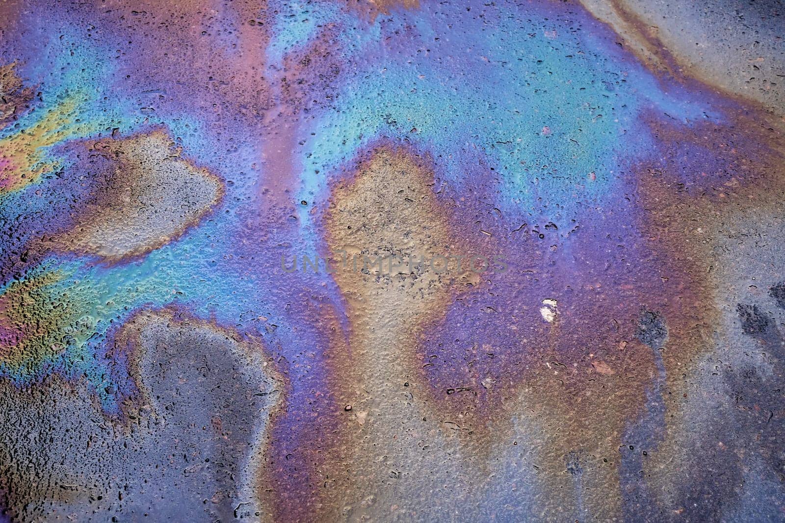 Multi-colored toxic stains of spilled gasoline on wet asphalt during the rain. Rain washed away car oil or fuel flowing from a faulty car in a parking lot.