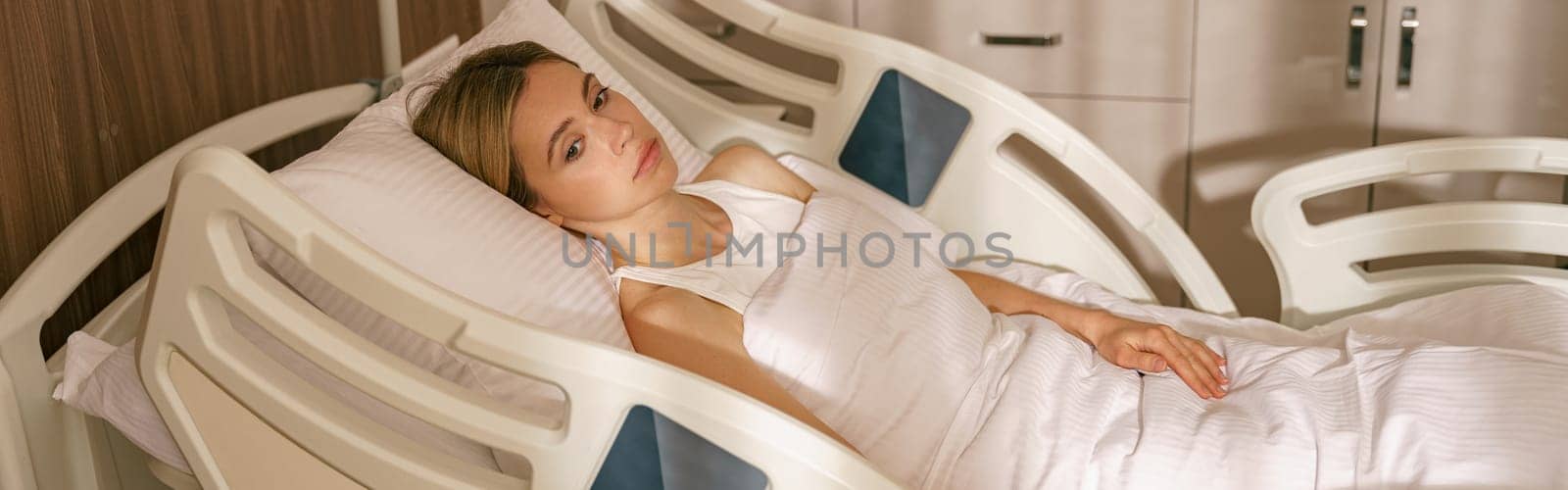 Young woman lying on bed at modern hospital ward after surgery. High quality photo