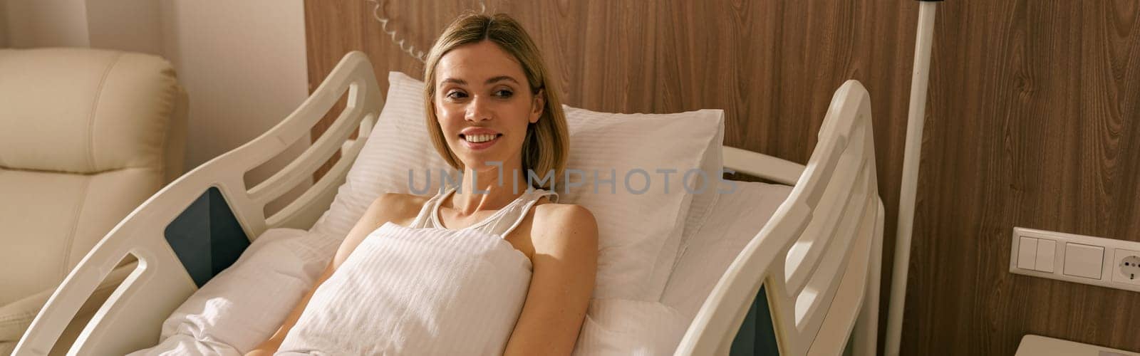 Smiling woman lying on bed at modern hospital ward after surgery. Health care and medicine concept by Yaroslav_astakhov