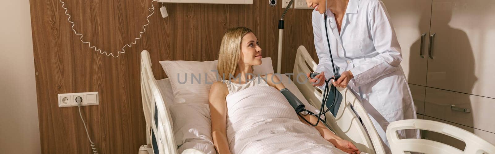 Doctor checking blood pressure of young woman patient in ward of modern clinic. High quality photo