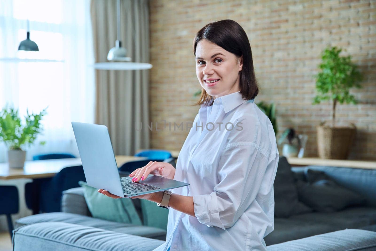 Young woman sitting on sofa using laptop for work, freelancing, learning by VH-studio