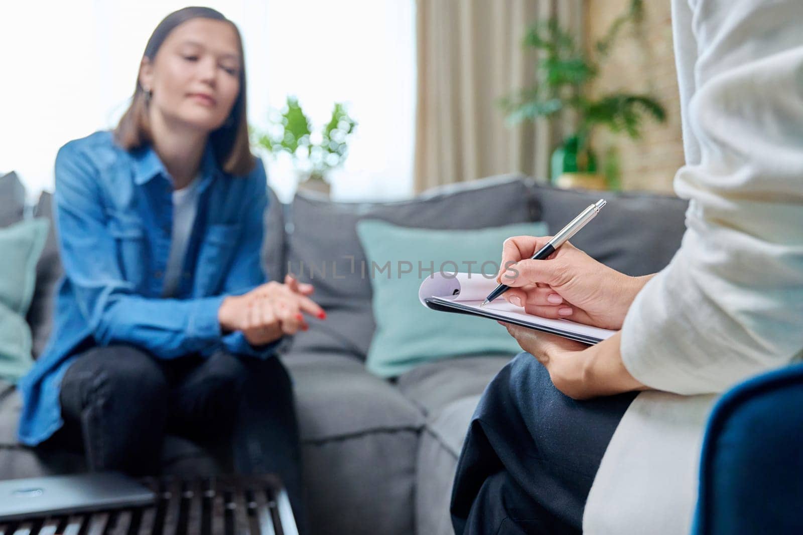 Workplace of counselor psychologist, close-up of hands female mental specialist with clipboard working with female patient. Psychology counseling treatment psychotherapy mental health youth concept