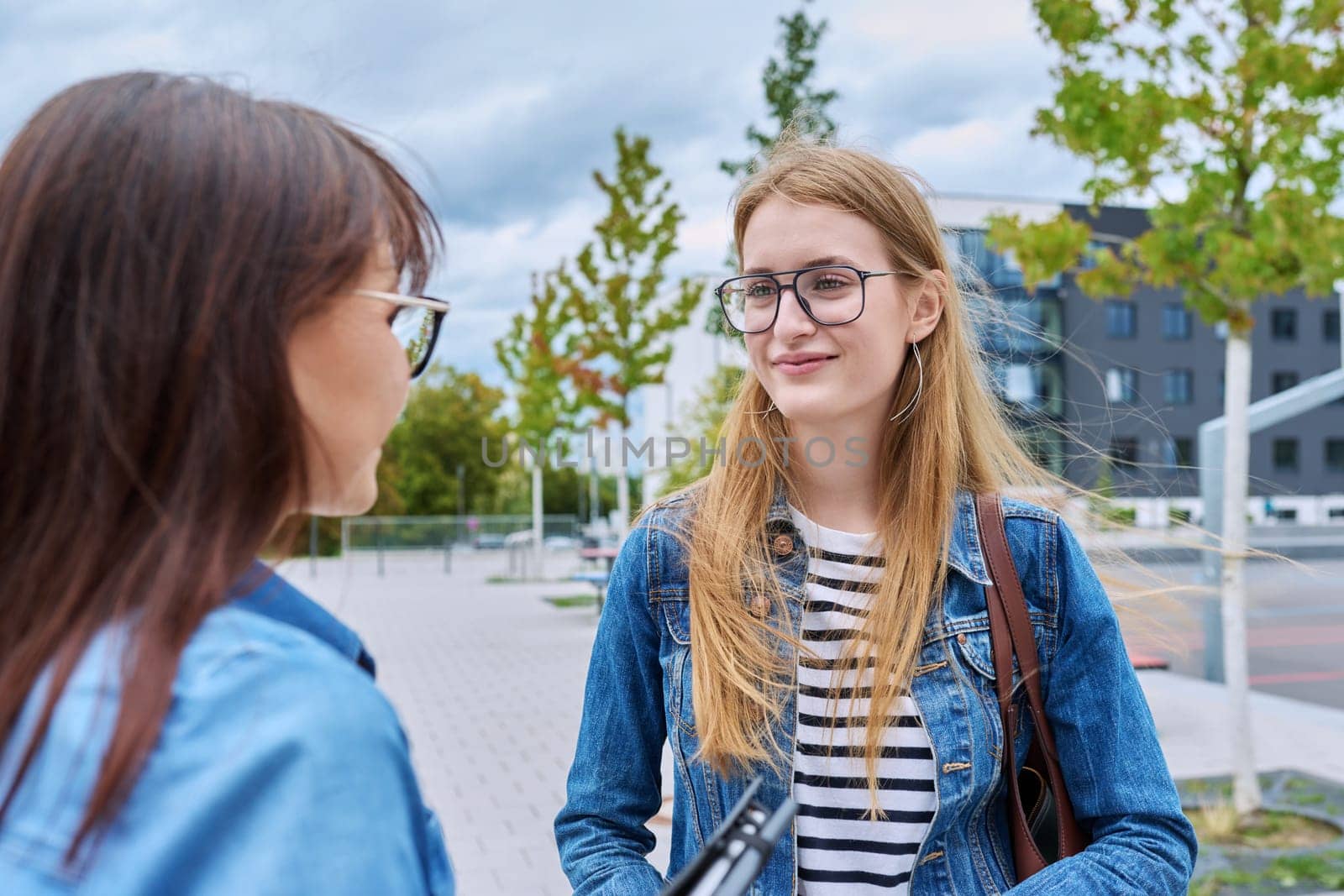 Teenage talking smiling girl looking at woman, outdoor.