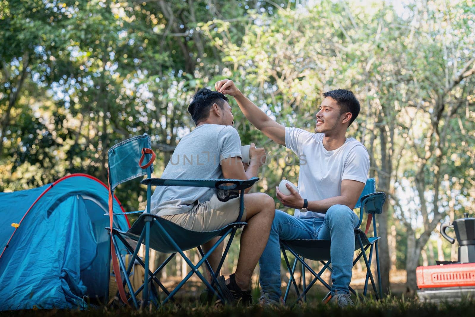 Male gay couple asian traveling with tent camping outdoor and various adventure lifestyle hiking active summer vacation. drinking coffee and talking together.