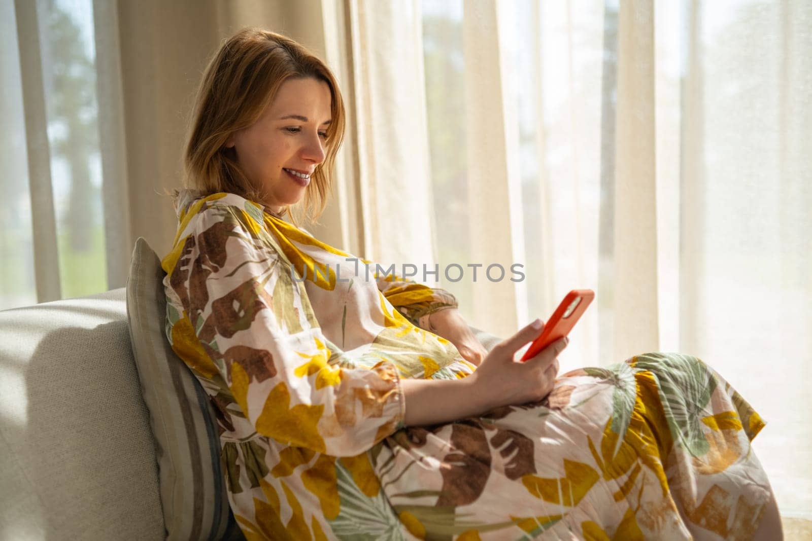 Pregnant joyful woman checks her smartphone relaxing on the sofa.
