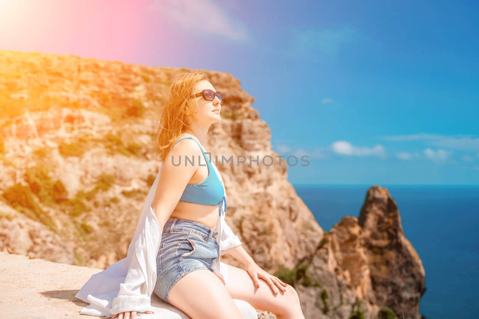 Woman travel summer sea. Portrait of a happy woman on a background of rocks and the sea. Side view of a woman in a white shirt and swimsuit. Freedom and happiness.