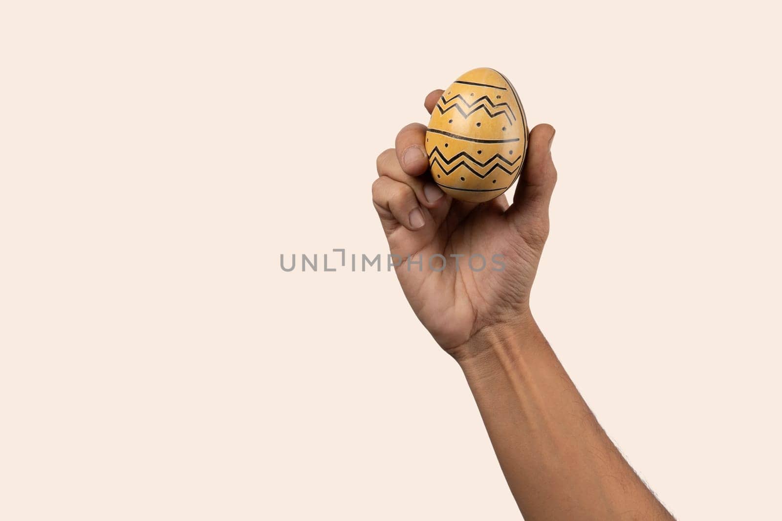 Male hand holding modern painted easter egg on beige background. High quality photo