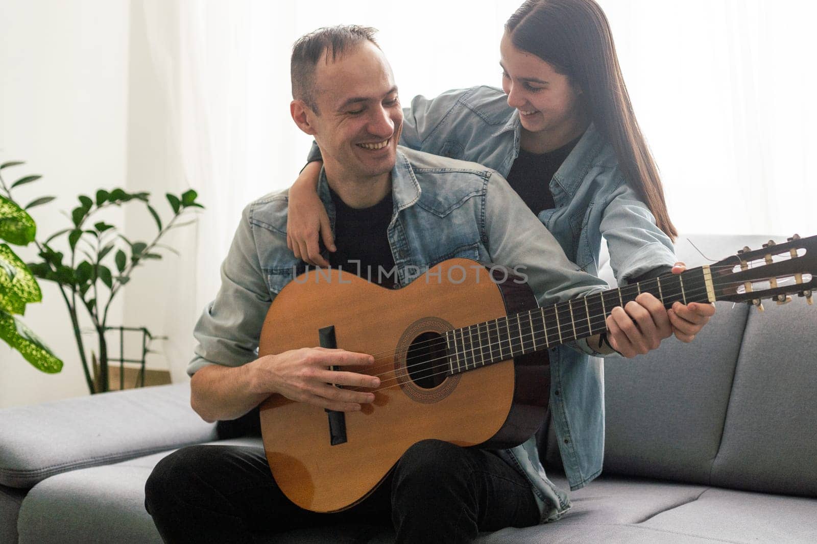 Father guy teaching girl teenager daughter guitar playing at home. Family musical lessons with strings instrument. High quality photo