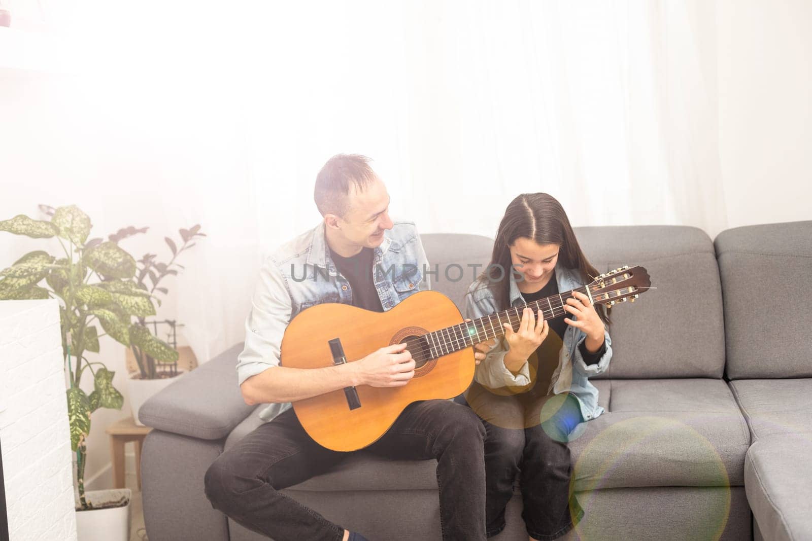 Father guy teaching girl teenager daughter guitar playing at home. Family musical lessons with strings instrument by Andelov13