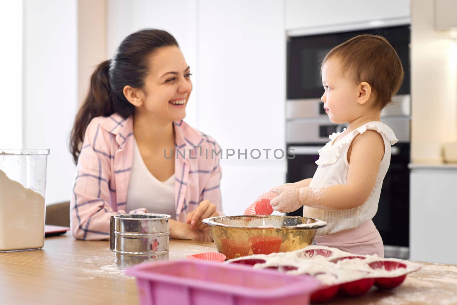 mother and little baby girl preparing the dough in the kitchen, bake cookies. happy time together
