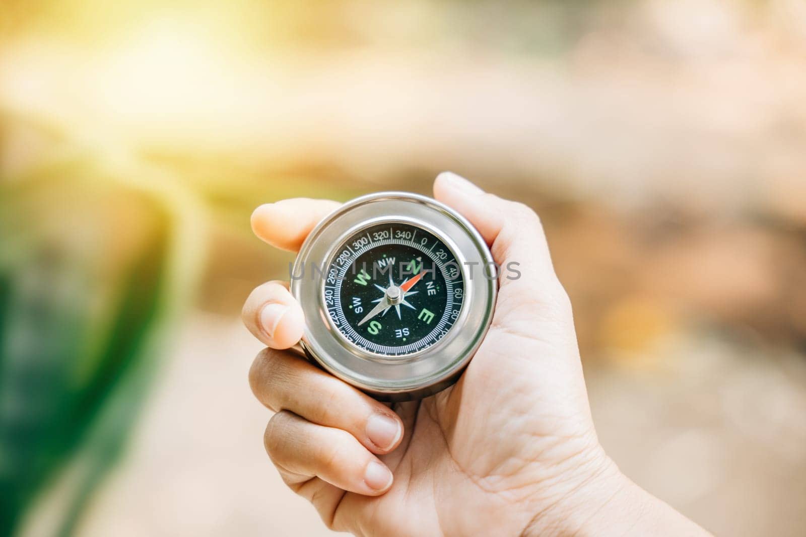 Hiker navigates the forest holding a compass to overcome confusion. The compass in the traveler hand signifies exploration and finding one path in the wilderness. by Sorapop