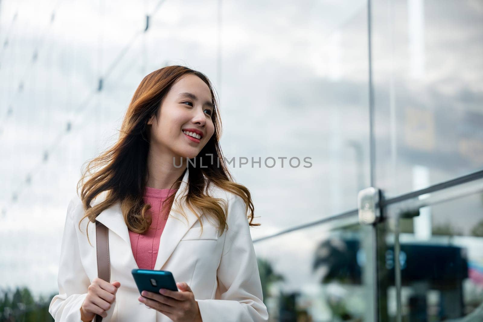 Asian businesswoman working with mobile phone standing against street front building near office by Sorapop