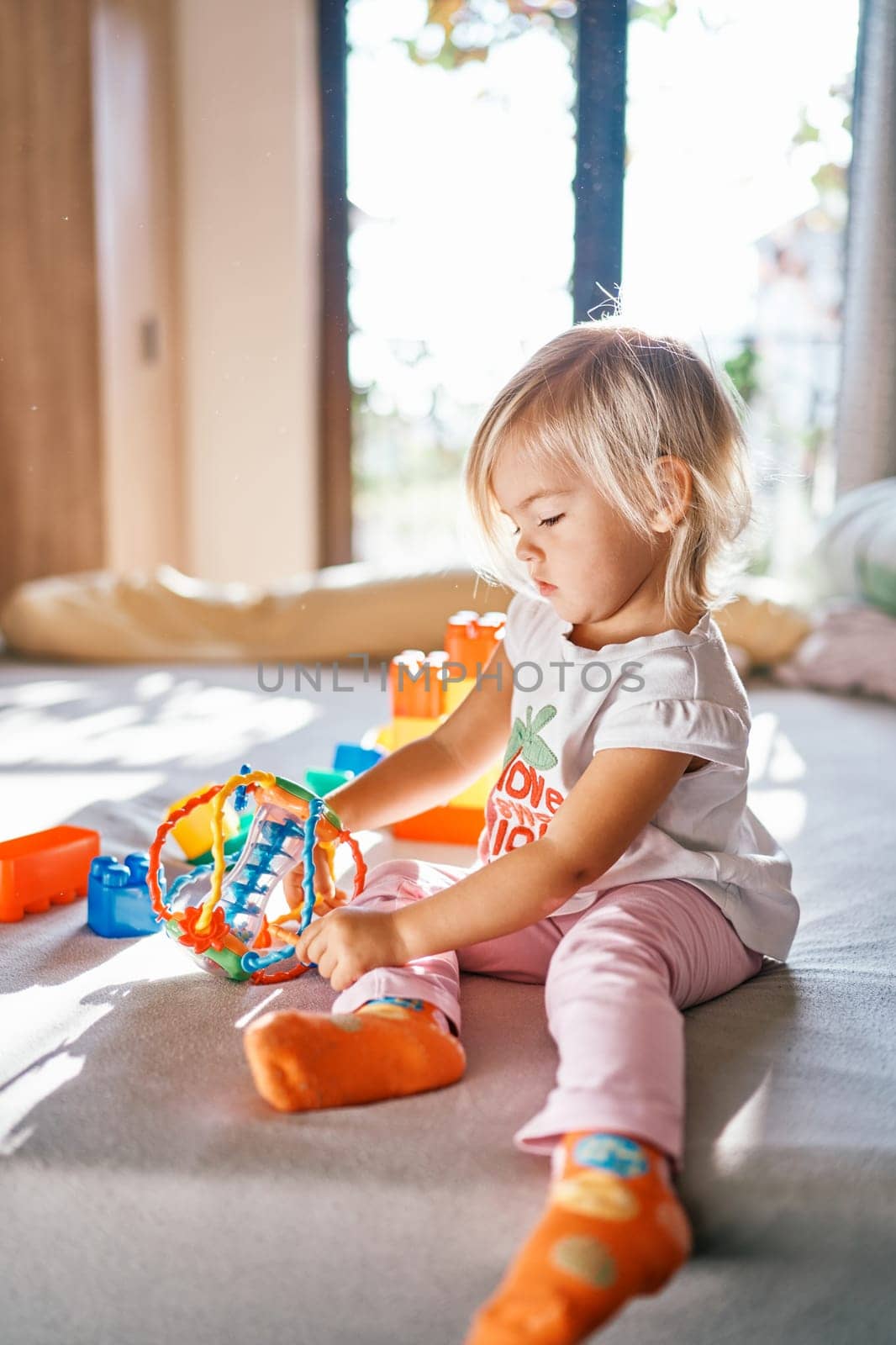 Little girl examines a round puzzle rattle while sitting on the bed. High quality photo