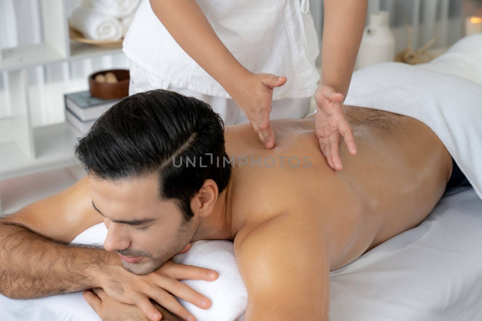 Caucasian man customer enjoying relaxing anti-stress spa massage and pampering with beauty skin recreation leisure in day light ambient salon spa at luxury resort or hotel. Quiescent