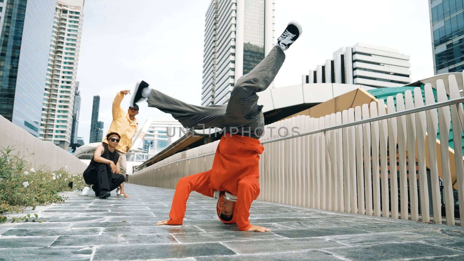 Young happy hipster perform break dancing or foot step with friend moving to hiphop music together. Skilled dancer doing freeze pose and waving hand. Modern lifestyle. Outdoor music 2024. Sprightly.