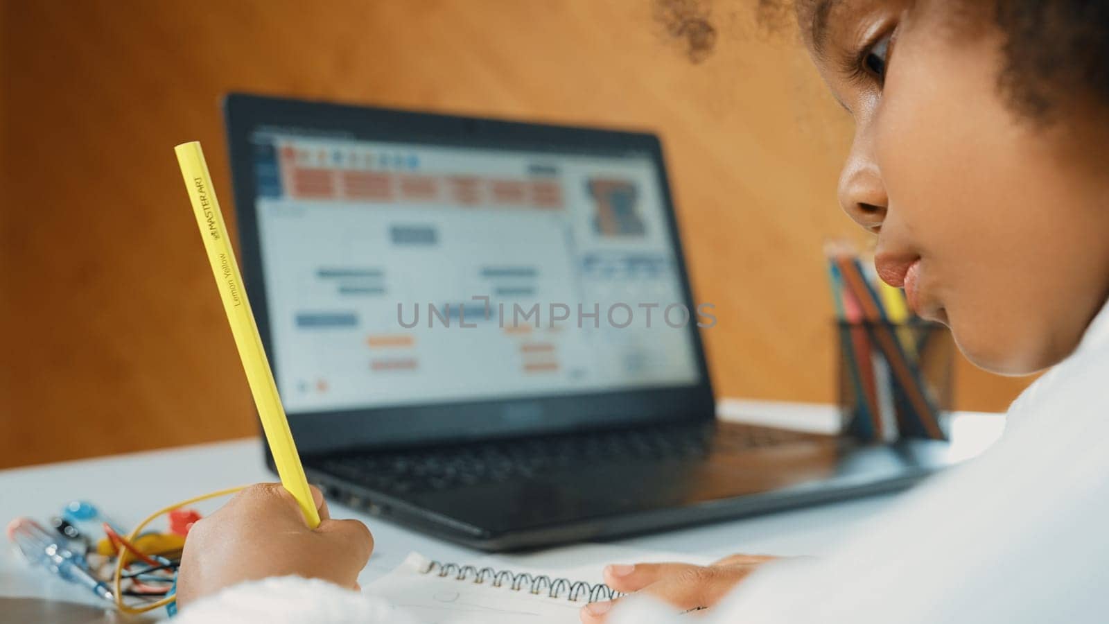 African girl moving touch pad while using laptop programing code and writing prompt code in STEM education. Children learning to designing setting engineering prompt at school. Top view. Erudition.