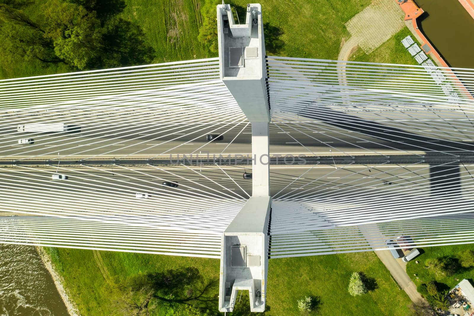 Cars drive on massive Redzinski Bridge over river with dark green water flowing near Wroclaw. Cable-stayed bridge above green island vertical aerial motion