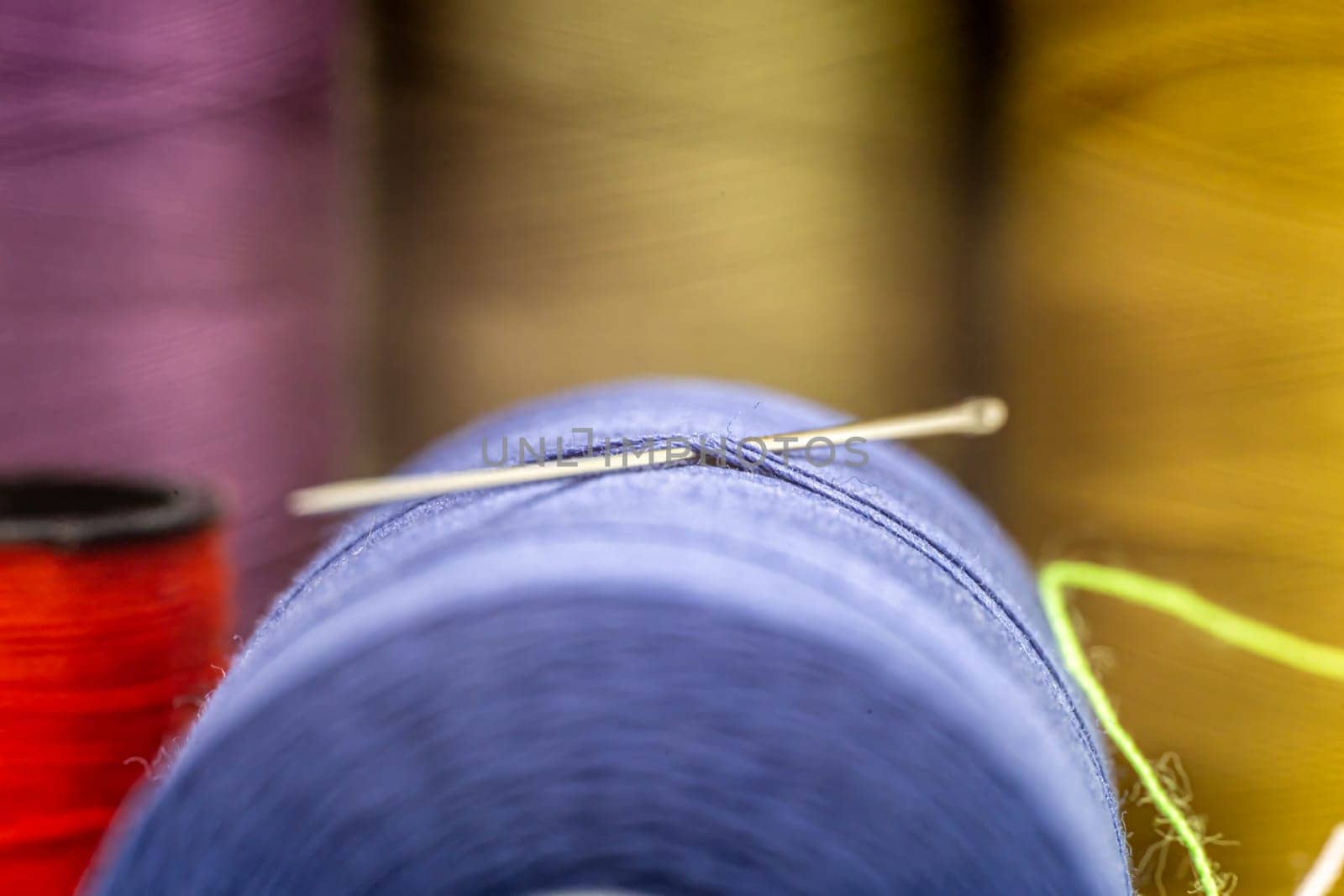 Closeup of a needle in a thread with other colorful needles in the blurry background by exndiver