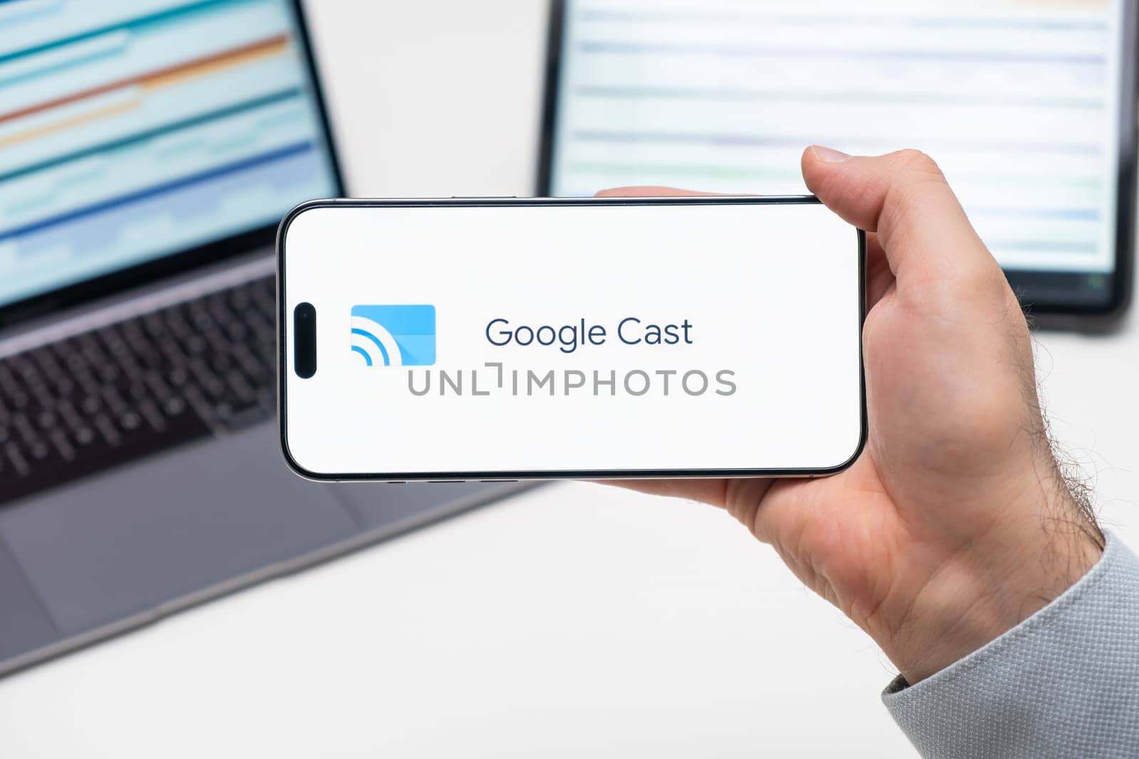 Google Cast logo of app on the screen of mobile phone held by man in front of the laptop and tablet, December 2023, Prague, Czech Republic