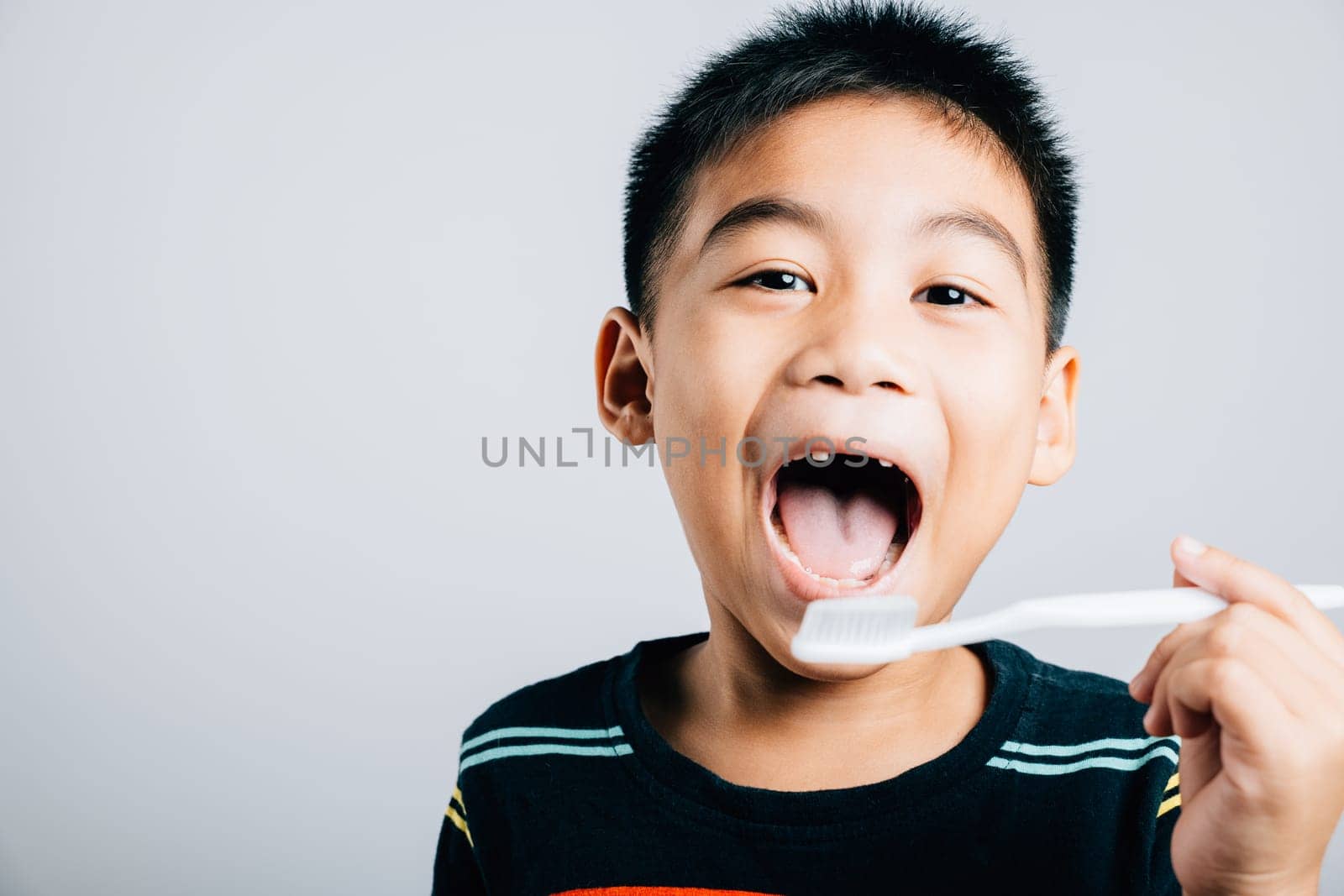 Isolated on a white background an Asian child without an upper milk tooth holds a toothbrush promoting dental hygiene routine and the joy of learning with a cheerful smile. Children dentist routine