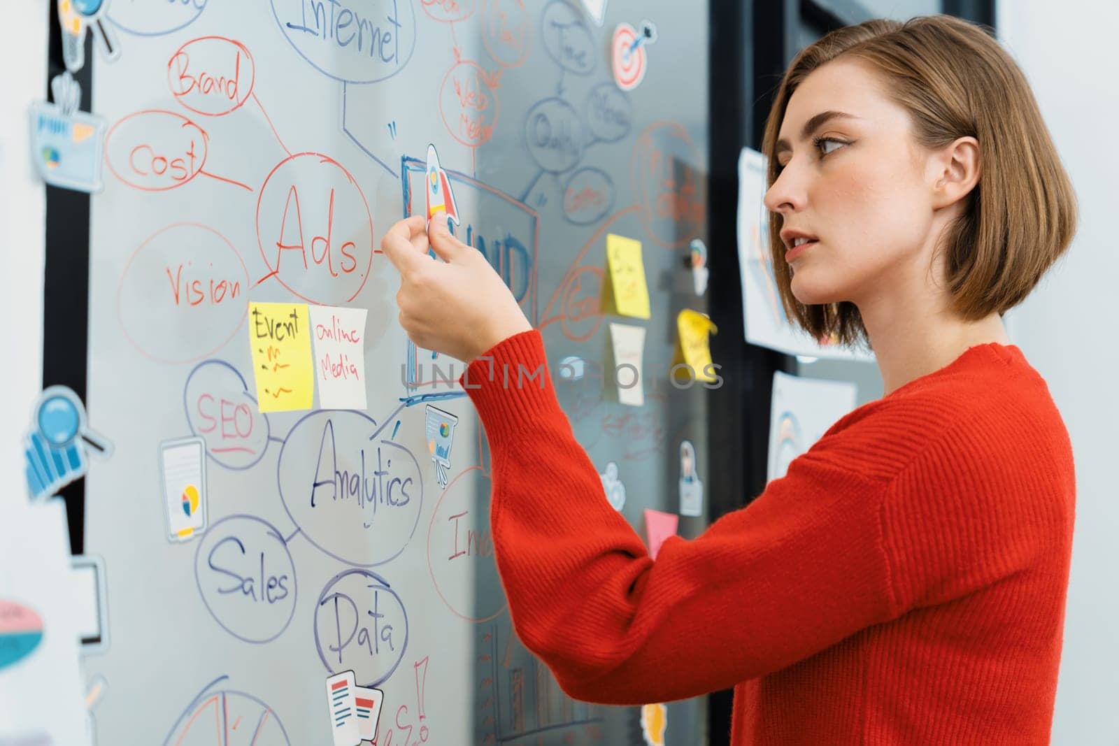 Professional attractive female leader sticks sticky note while presents creative marketing plan by using brainstorming mind mapping statistic graph at modern business meeting room. Immaculate.