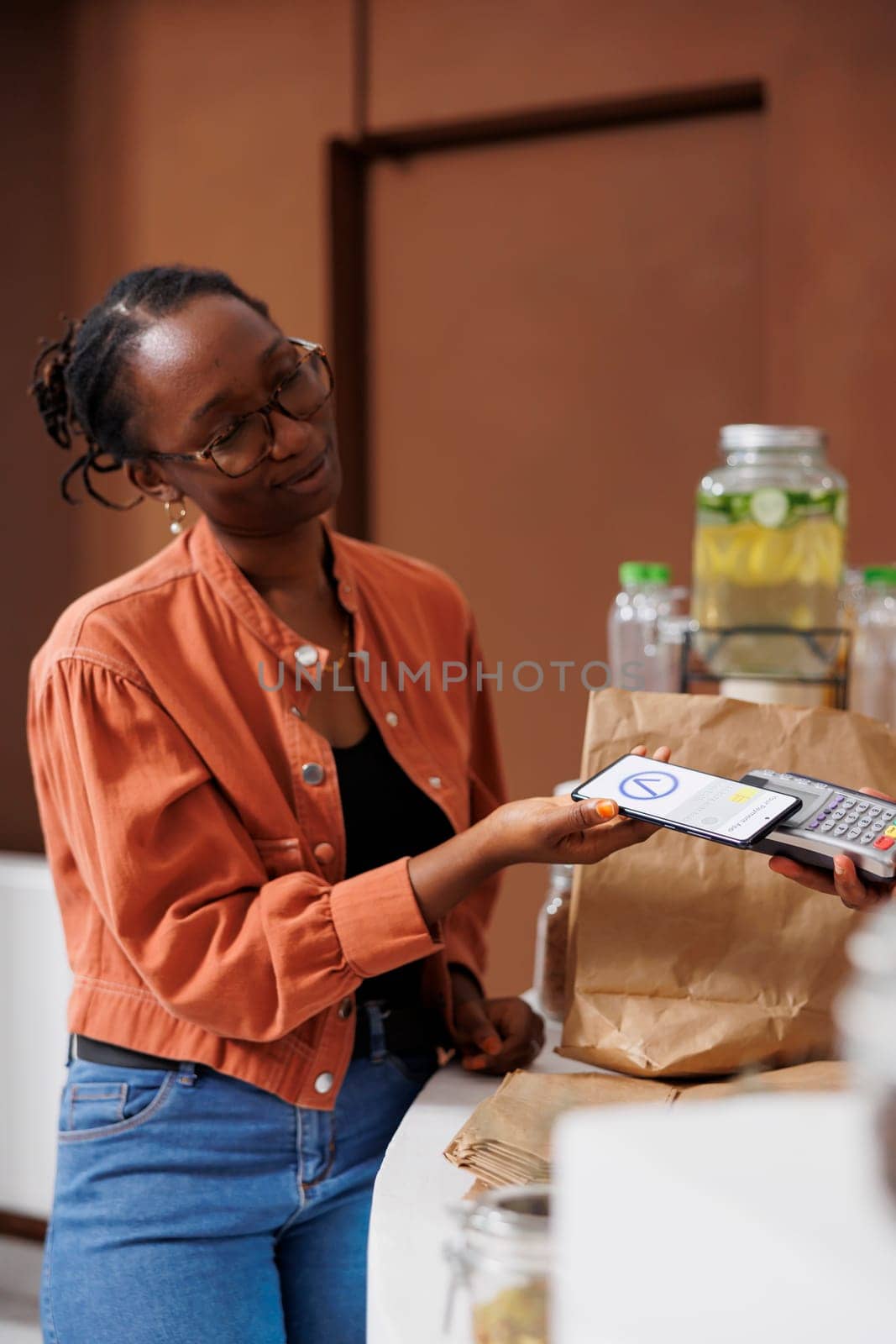 African American woman pays for her bio food using contactless payment on her mobile device. She holds a smartphone and supports cashless transactions at the locally grown market.