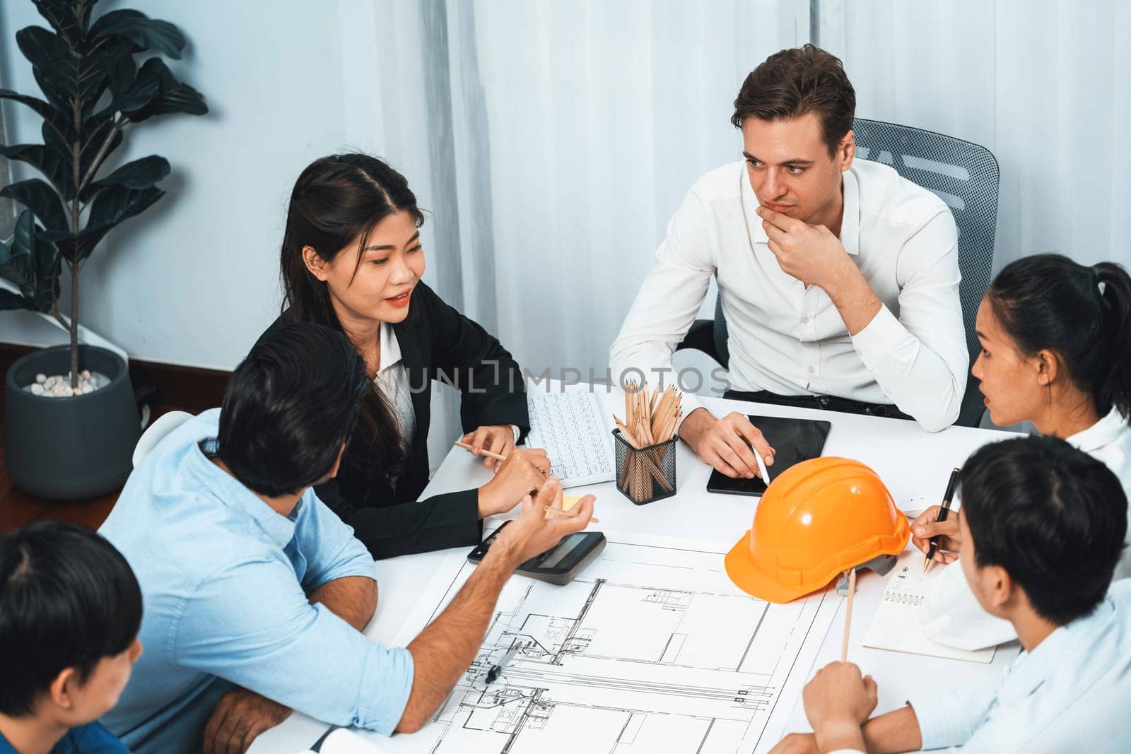 Diverse group of civil engineer and client working together on architectural project, reviewing construction plan and building blueprint at meeting table. Prudent