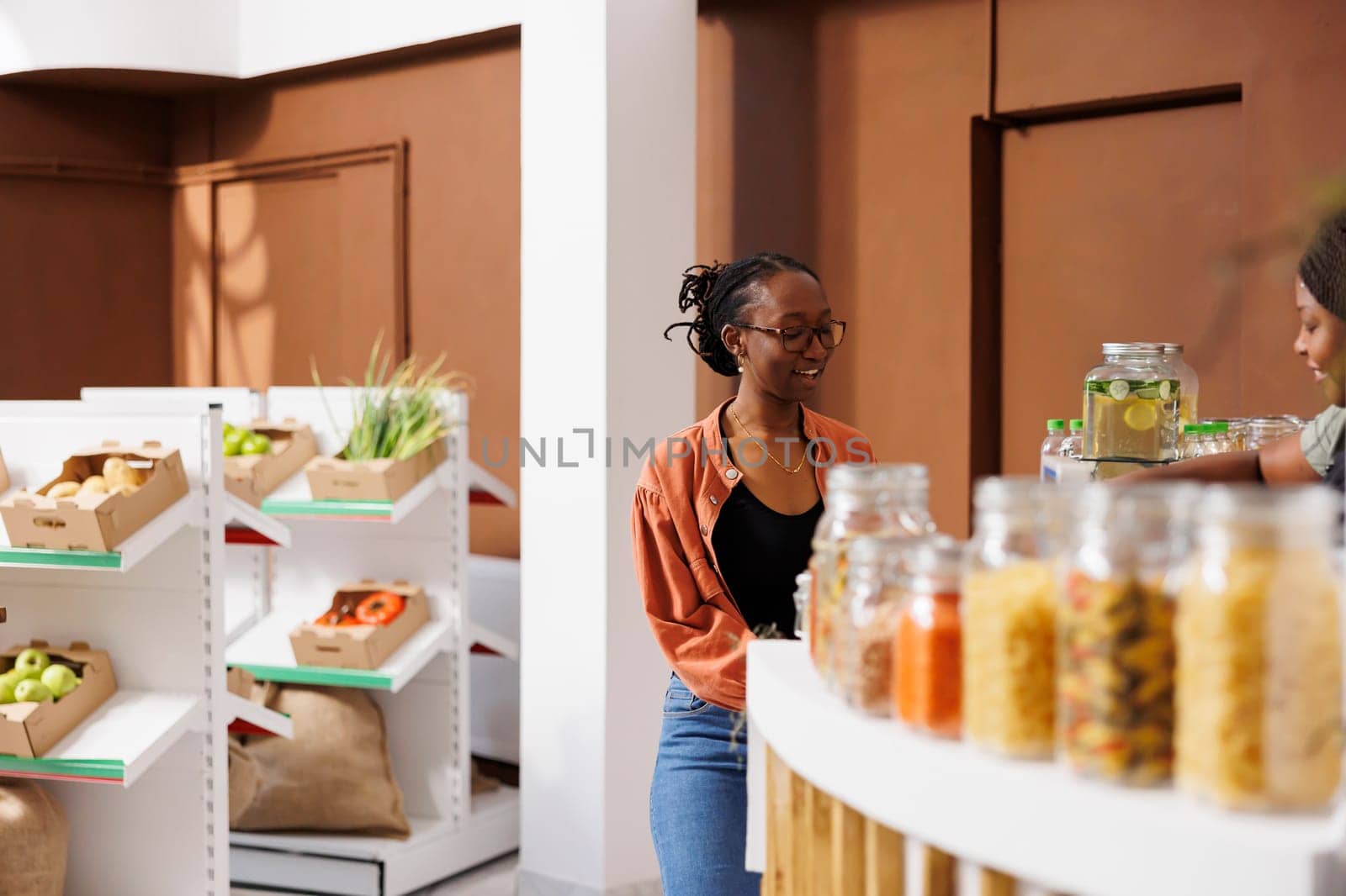 Portrait of african american female shopper standing at checkout counter, speaking with shopkeeper. Young lady with glasses waiting for her sustainable organic packaged products.