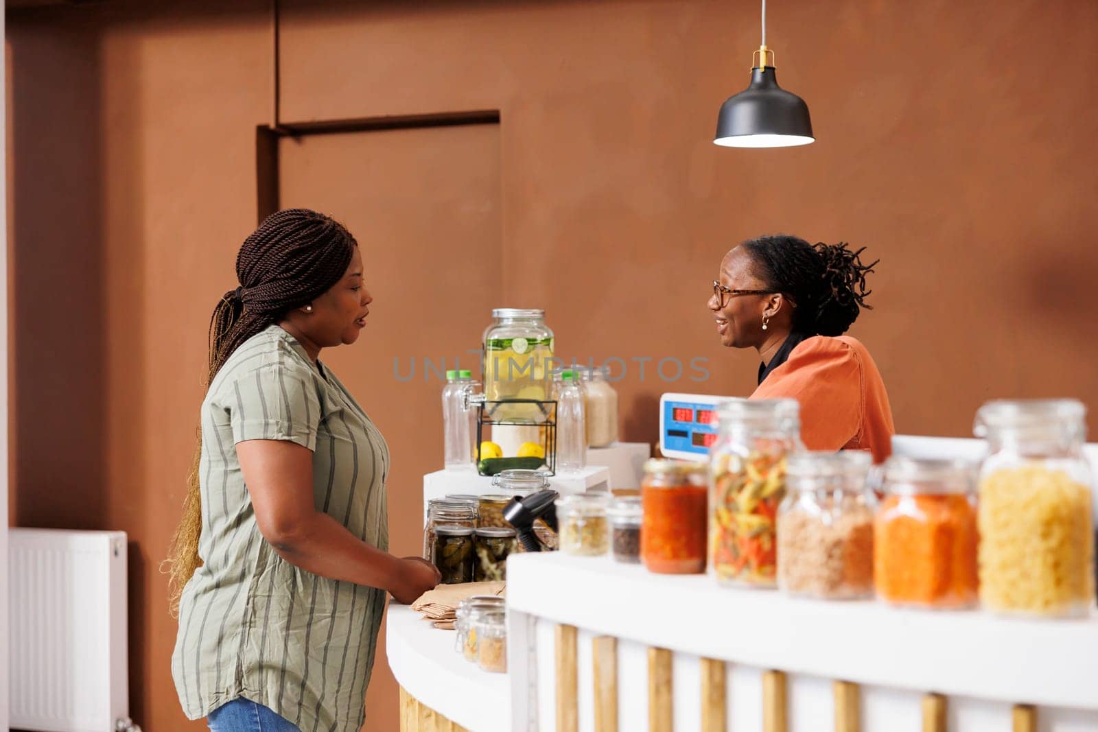 Vendor assisting female client with nutritious products. Cashier at eco friendly store promotes healthy lifestyle, offering fresh locally grown organic produce and sustainable, zero waste options.