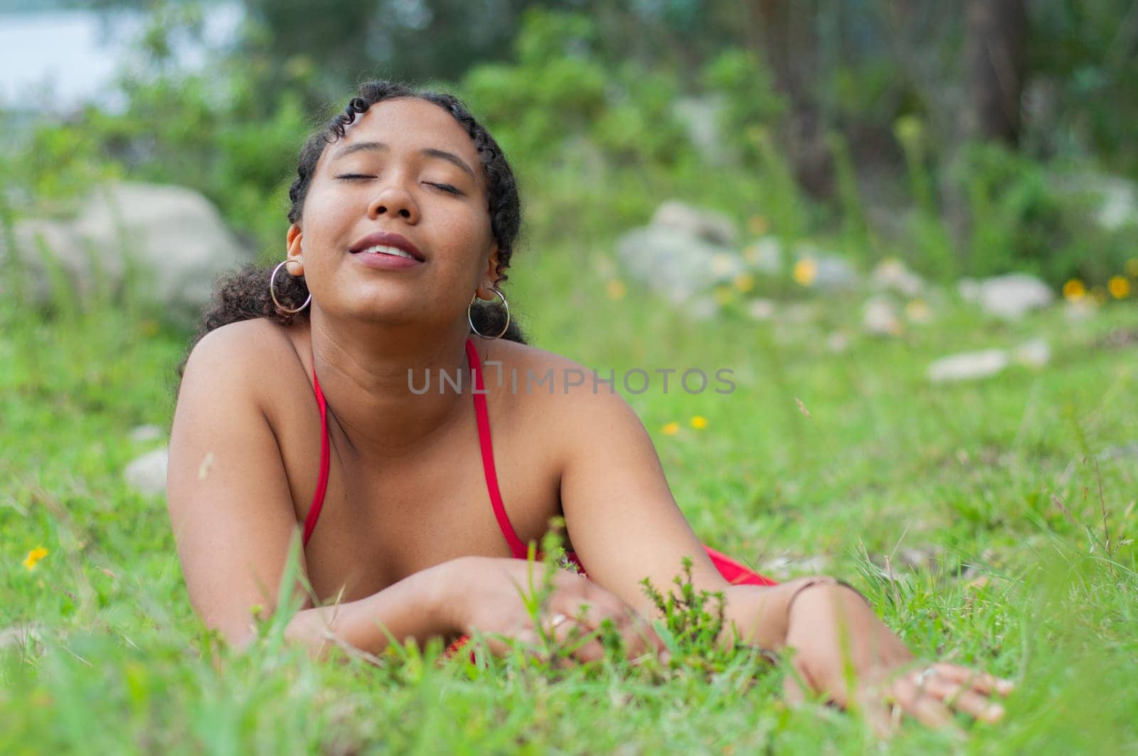 an attractive young woman lying on the grass of the field in a red dress with a face of pleasure and sensuality. earth day. High quality photo