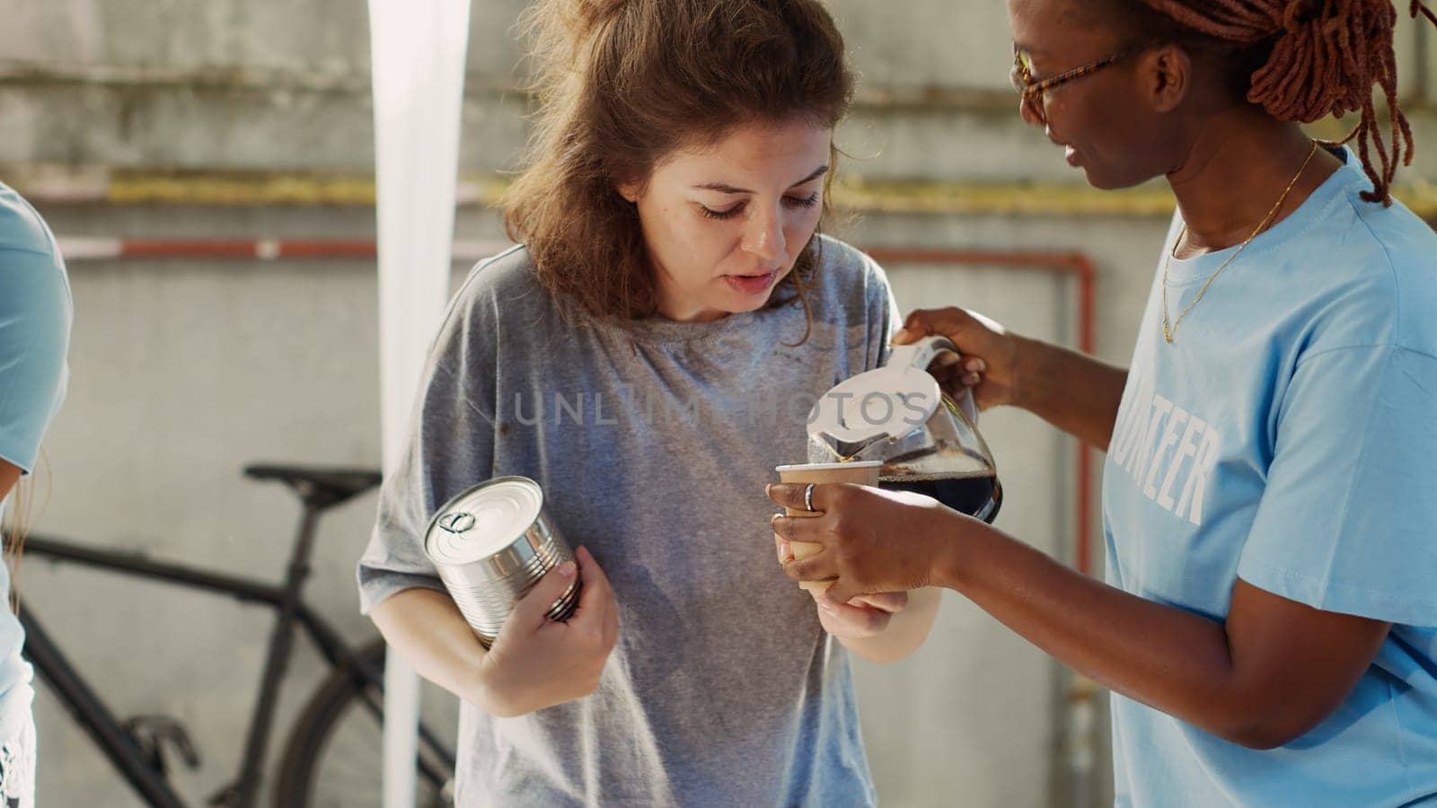Detailed view of african american female volunteer serving a cup of coffee to homeless caucasian lady. Friendly black woman at outdoor food bank sharing nourishments to the needy and less fortunate.