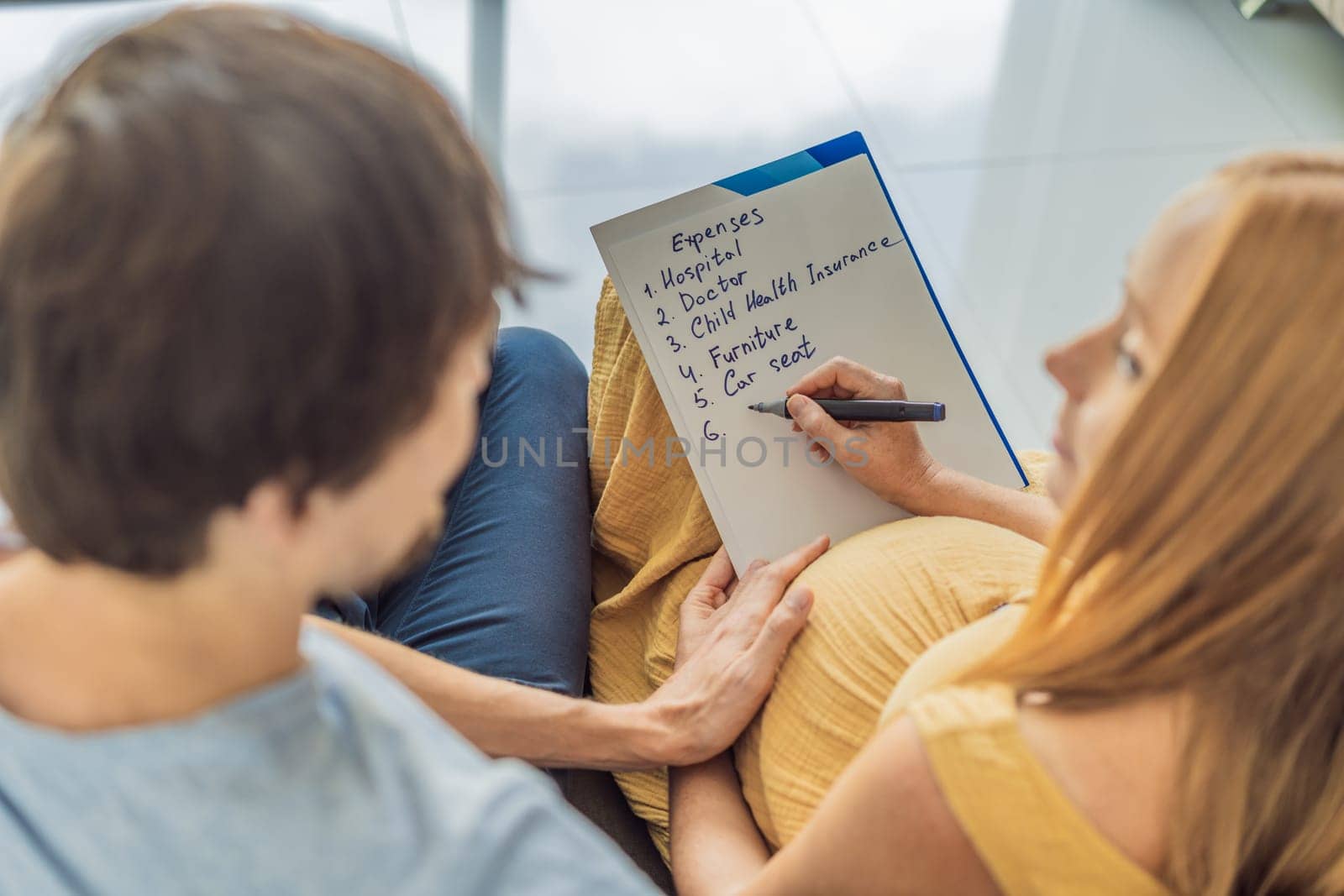 Expectant woman and her husband diligently compiles a list of childbirth costs, planning and organizing financial considerations for the upcoming delivery by galitskaya