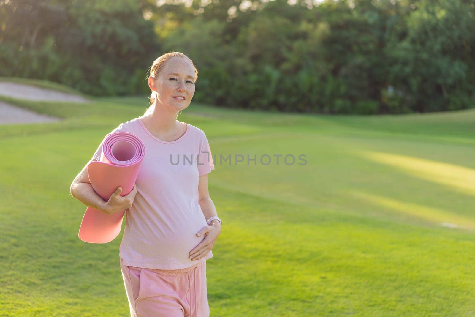 Energetic pregnant woman takes her workout outdoors, using an exercise mat for a refreshing and health-conscious outdoor exercise session.