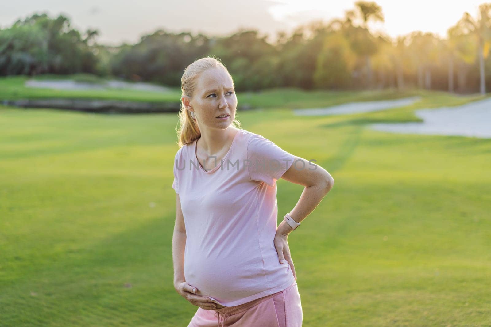 Expectant woman experiences back pain outdoors, seeking relief and comfort during pregnancy with a gentle outdoor stretch or rest by galitskaya