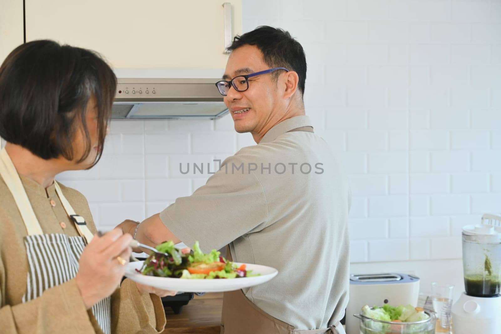 Attractive senior couple enjoying a healthy lunch in cozy kitchen interior. Retirement and healthy eating concept by prathanchorruangsak