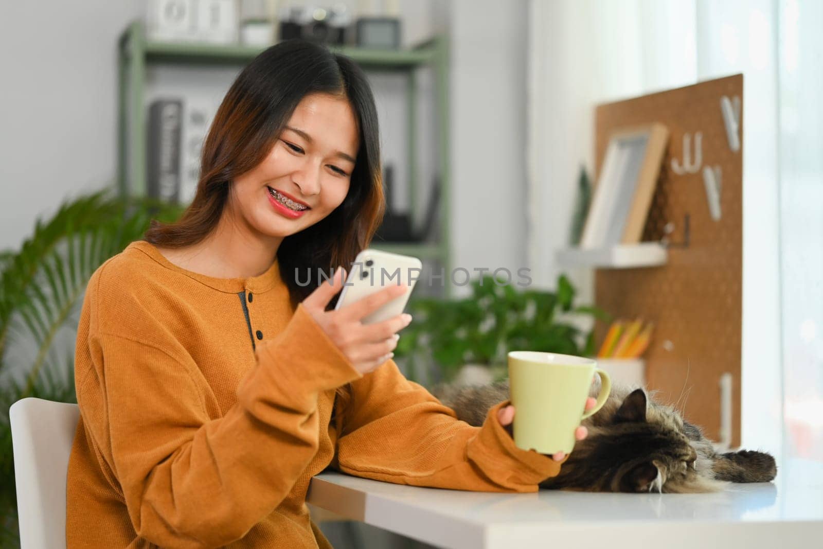 Cheerful young woman drinking coffee and reading text message on smartphone. by prathanchorruangsak