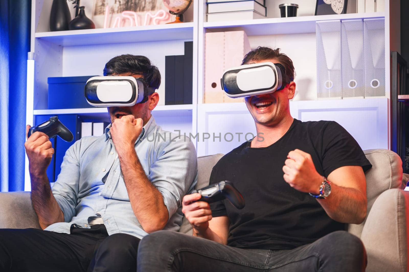 Buddy friend gamers playing video game using joysticks and VR headset of virtual technology in reality in studio room with neon blue light. Comfy living indoor with cheerful fighting winner. Sellable.