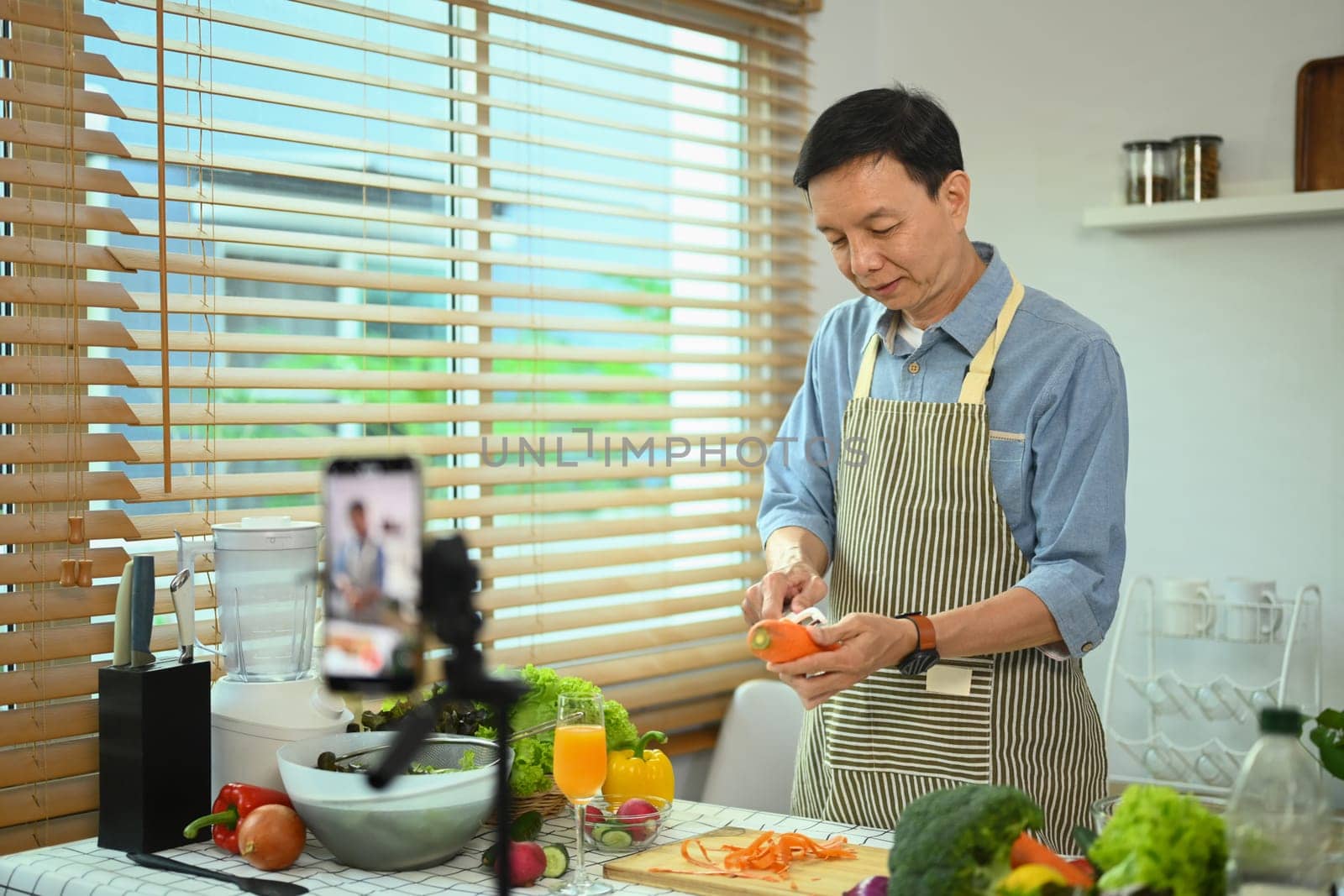 Active middle age man recording video blog about healthy nutrition on smartphone in kitchen.