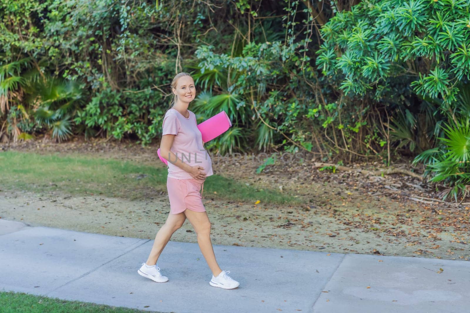 Energetic pregnant woman takes her workout outdoors, using an exercise mat for a refreshing and health-conscious outdoor exercise session by galitskaya