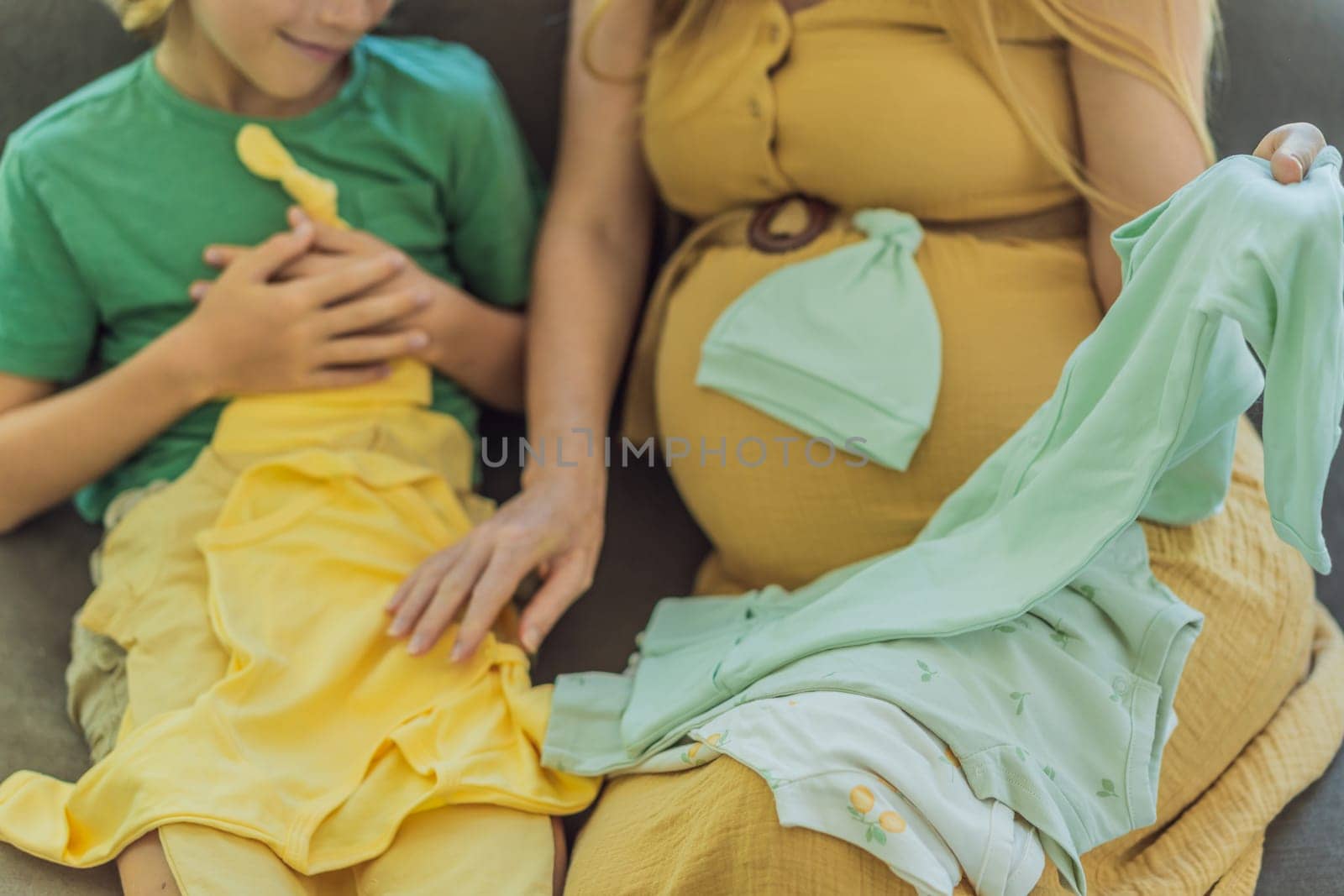 Heartwarming family moment as expectant mom and son joyfully browse through newborn baby's clothes, eagerly anticipating the arrival of a new family member.