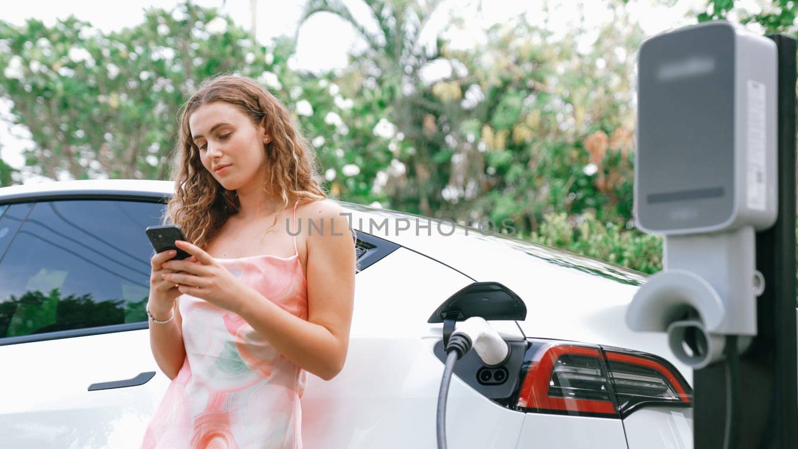 Young woman use smartphone to pay for electricity for EV car. Synchronos by biancoblue