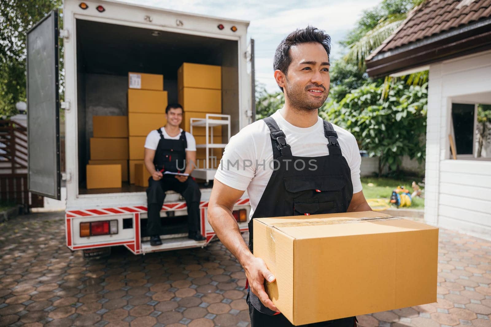 Young delivery men unload boxes outdoors. Movers cooperate in relocation service. Teamwork among colleagues. Smiling workers carrying boxes. relocation cooperation Moving Day